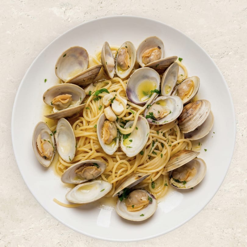 Spaghetti alle Vongole, a pasta dish with clams, garlic, and parsley on a white plate.