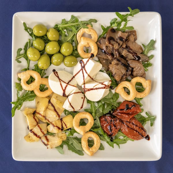 A Milane Italian antipasto platter with olives, mozzarella, artichokes, sun-dried tomatoes, and taralli on arugula.