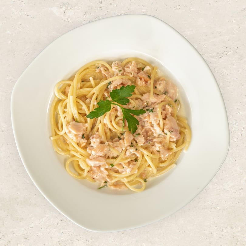 Spaghetti with salmon and cream sauce, garnished with parsley, on a white plate.