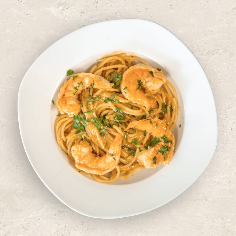 Spaghetti with shrimp and parsley in a creamy orange sauce, served on a white plate.