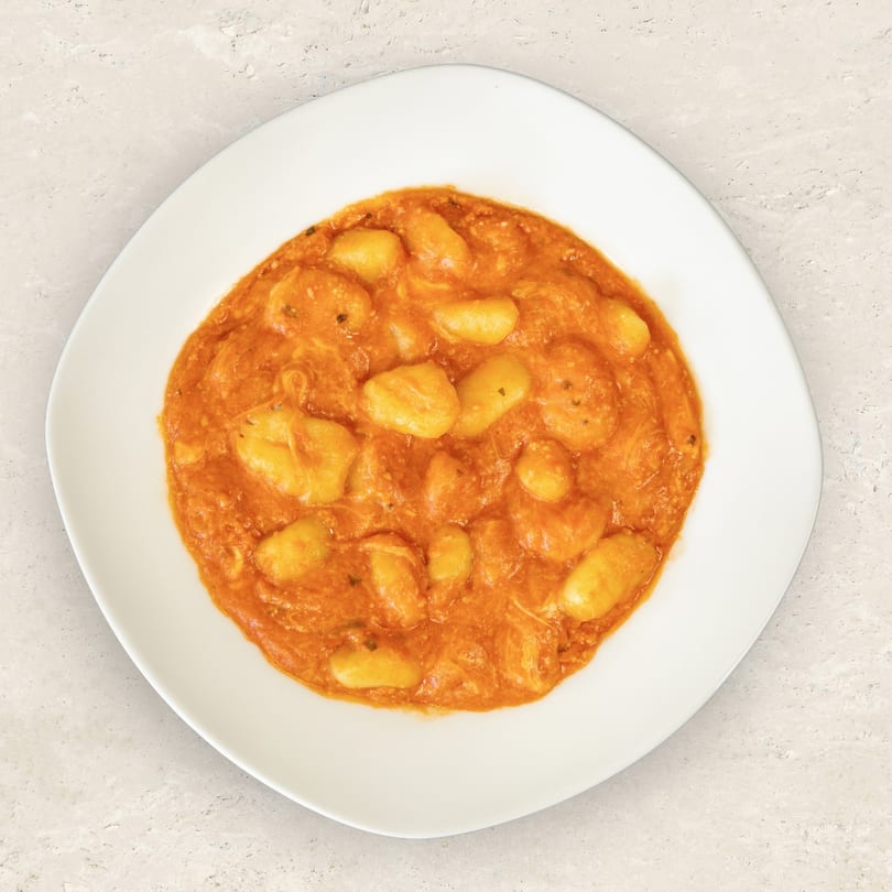 A white plate filled with gnocchi in a rich, orange-red tomato sauce, viewed from above.