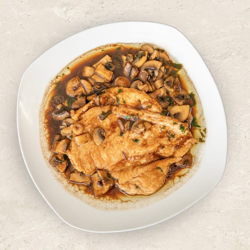 Chicken cutlets in a rich brown sauce with sliced mushrooms and herbs on a white plate.