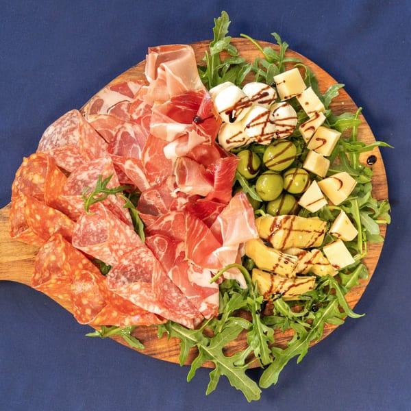 Milane's Italian charcuterie board with various meats, cheeses, olives, and artichokes on arugula.