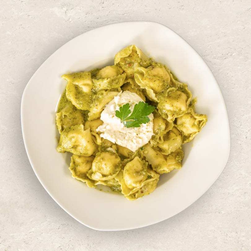Tortellini pasta with green pesto sauce, topped with a dollop of ricotta cheese and parsley.
