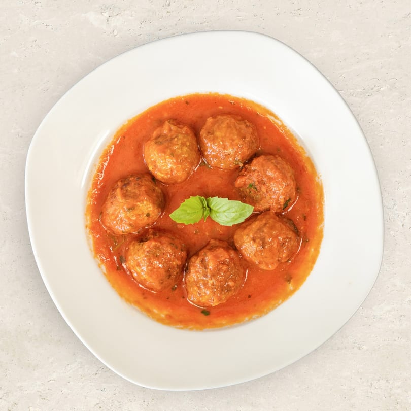 Seven meatballs in a rich red tomato sauce, garnished with fresh basil, on a white plate.
