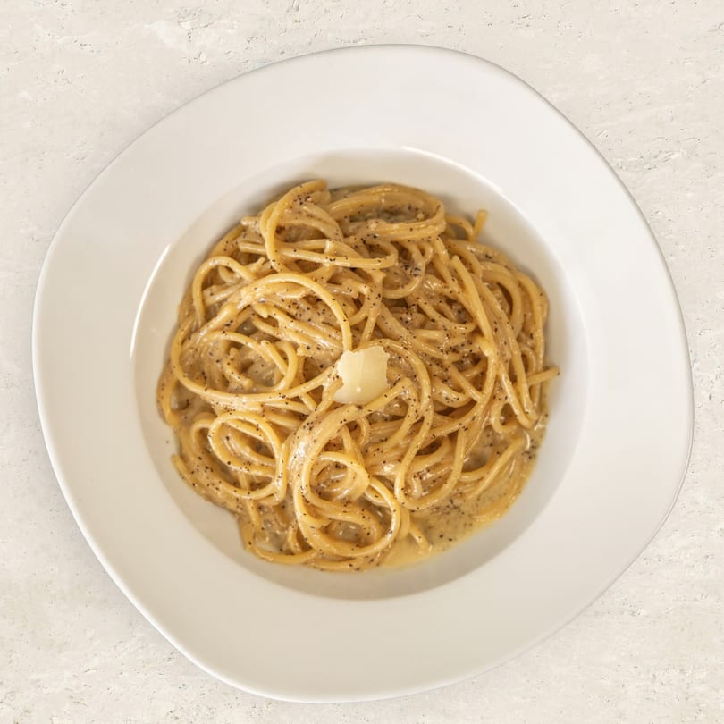 Cacio e pepe pasta with black pepper and a dollop of cheese in a white bowl.