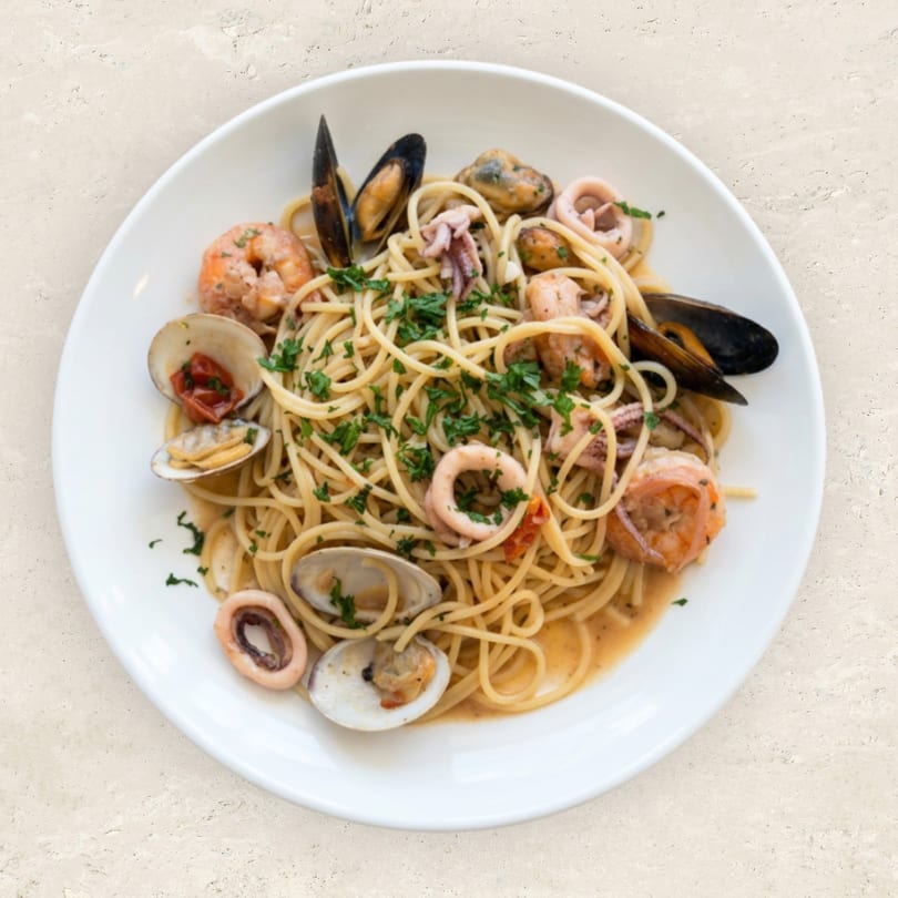 Spaghetti with shrimp, mussels, clams, and calamari, garnished with fresh parsley on a white plate.