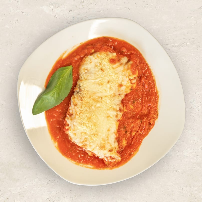 Chicken parmesan with melted cheese and tomato sauce, garnished with a fresh basil leaf.