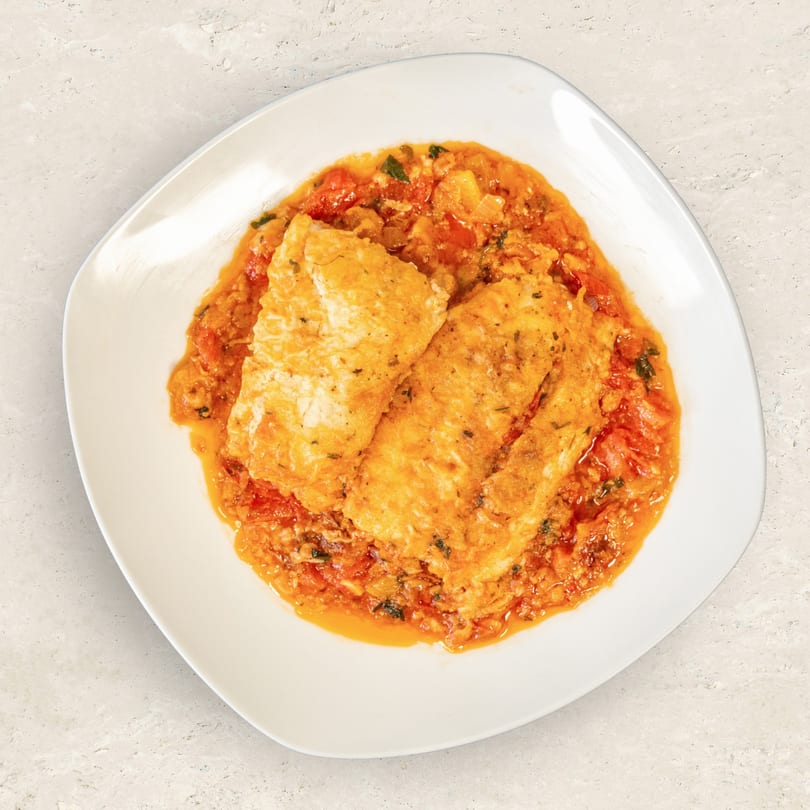 Two pieces of golden-brown fish fillets in a rich tomato and herb sauce on a white plate.